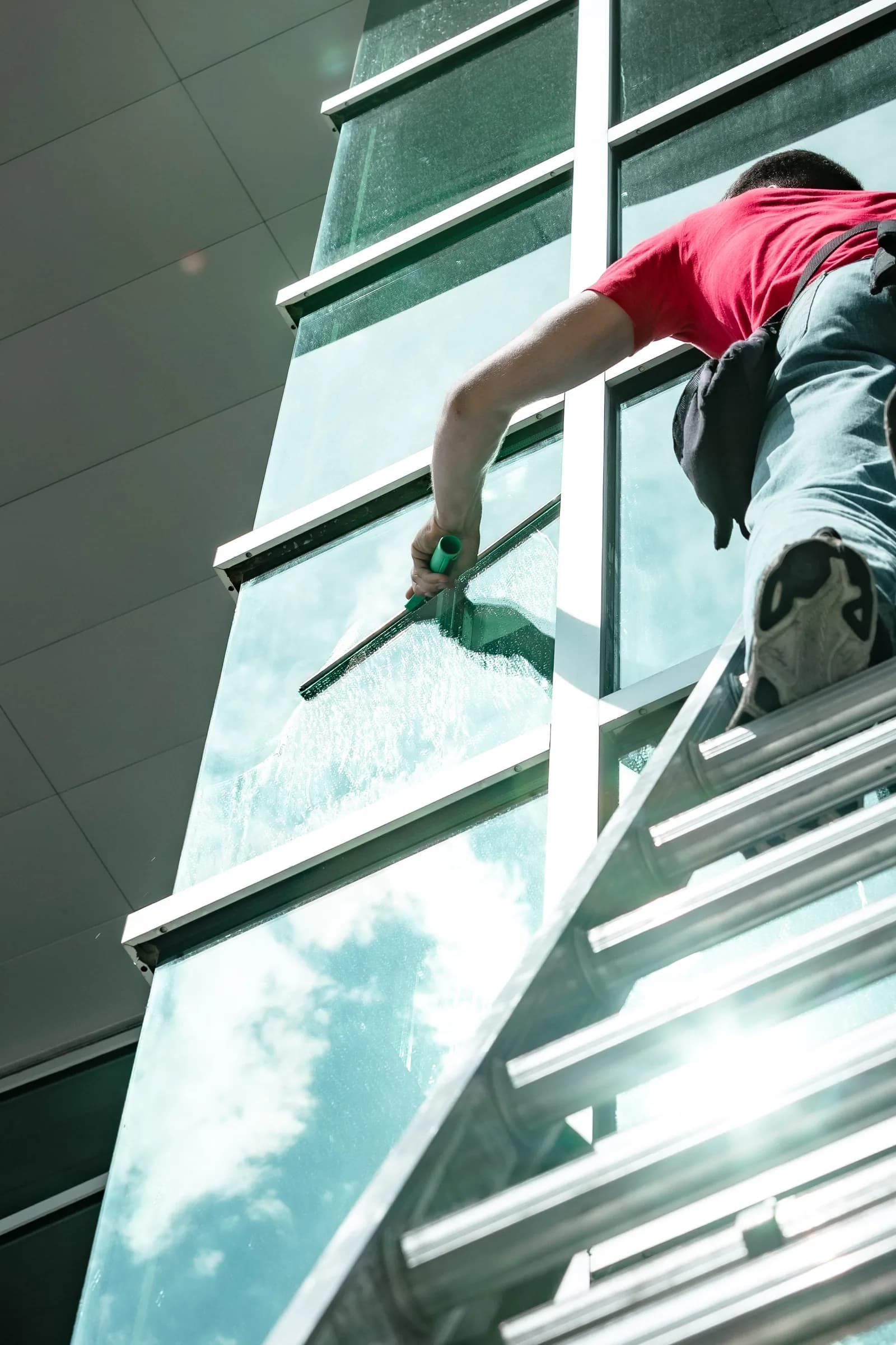 Sonlight technician on a tall ladder cleaning commercial windows in Colorado — Broomfield, Colorado